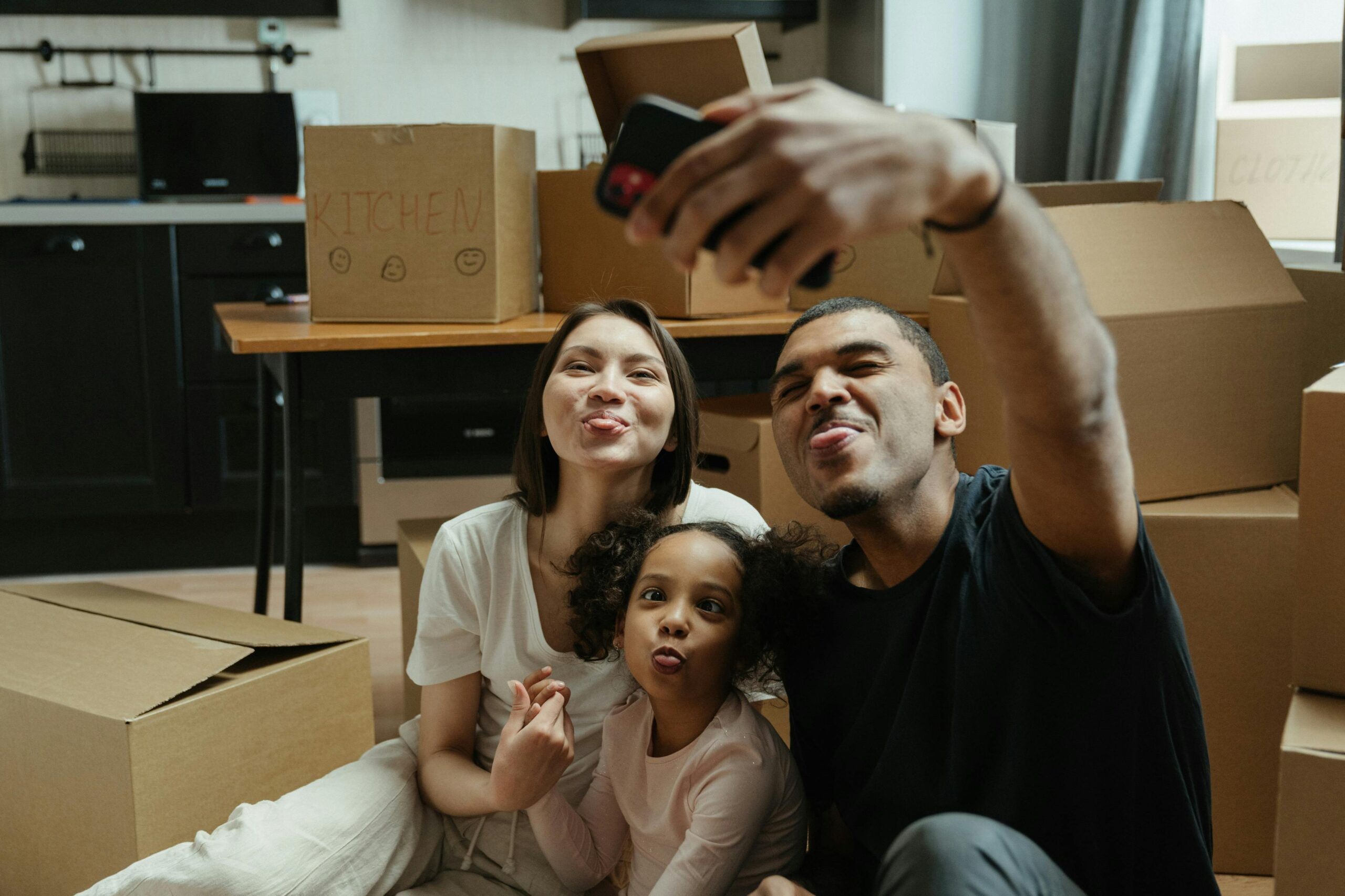 Happy family capturing a selfie surrounded by moving boxes, embracing their new home adventure.